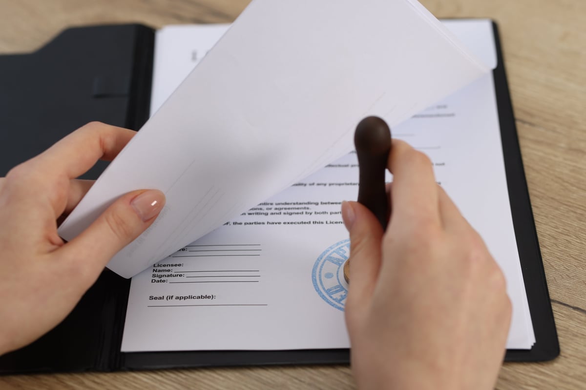 Woman stamping licensing agreement document at wooden table